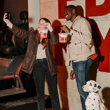 Two people holding popcorn buckets and taking a selfie, with a Dalmatian sitting nearby, in a modern indoor setting.