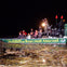Group of people on a "Boggy Creek Airboat Rides" airboat at night, surrounded by water and reeds, with a guide standing.