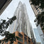 A tall, modern skyscraper with a unique, wavy design against a cloudy sky, surrounded by trees and other buildings.