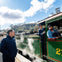 Two train operators stand beside and inside a green steam locomotive at a station, with a person observing nearby.