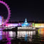 A lit-up Uber Boat on the Thames at night with illuminated London buildings and the London Eye in the background.
