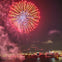 Bright fireworks exploding in the night sky over a cityscape, with buildings and a waterfront visible below.