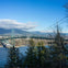 A suspension bridge spans over a body of water, surrounded by trees and mountains under a clear blue sky.