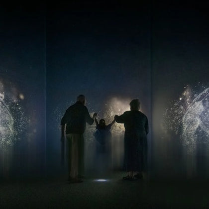 People interacting with an immersive digital art installation featuring illuminated light patterns in a dark room.