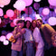 Four people taking a selfie surrounded by colorful glowing spheres in a vibrant, atmospheric space.