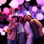 Four people pose for a selfie in a dimly lit room filled with hanging, glowing pink and white spherical lights.