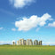 Stonehenge under a blue sky with scattered clouds, surrounded by green grass.