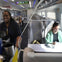 A smiling staff member serves refreshments on a modern train; passengers are seated, one working on a laptop.