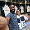 A smiling man and woman take a selfie in a locker room with Tottenham Hotspur jerseys hanging in the background.
