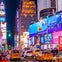Bustling Times Square at night with bright advertising billboards, heavy traffic, yellow taxis, and crowded sidewalks.