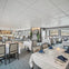 A modern restaurant interior with neatly arranged tables, white tablecloths, and blue napkins, featuring large windows and a bar area.
