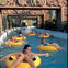 People floating on yellow inner tubes in a water ride surrounded by decorative stone structures and greenery.