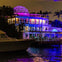 A brightly lit modern building by the water at night, with colorful lights and a geodesic dome on the roof.