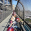 A group of people wearing red helmets, standing on a fenced walkway of a bridge, looking down at the scene below.
