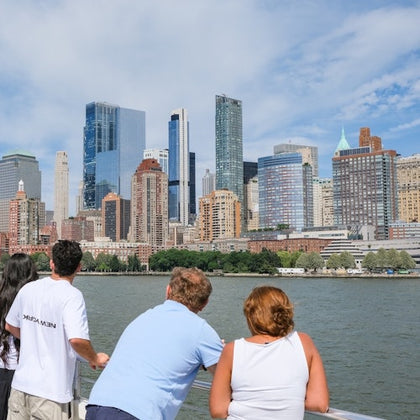 Four people stand by a railing, looking at a city skyline across the water on a clear day.