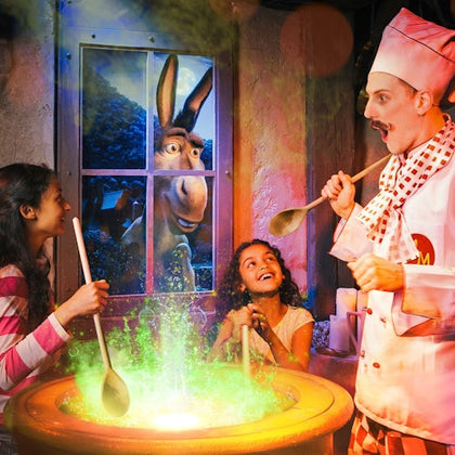 Two children and a chef stir a cauldron with green liquid, while a donkey looks in through the window, smiling.