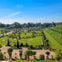 A formal garden with neatly trimmed hedges, potted plants, gravel paths, and manicured lawns under a clear blue sky.