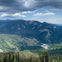 A mountainous landscape with lush greenery, forested areas, and clouds in the sky.
