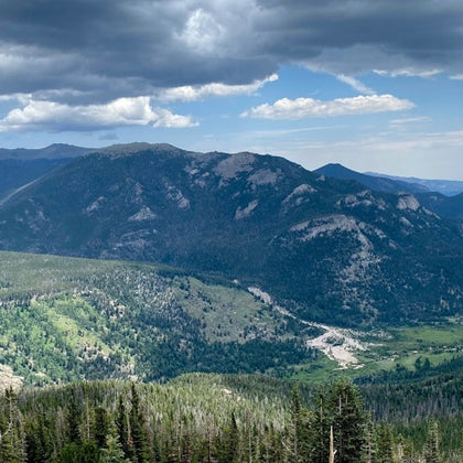 A mountainous landscape with lush greenery, forested areas, and clouds in the sky.