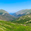 A scenic view of a green valley surrounded by mountains under a clear blue sky.