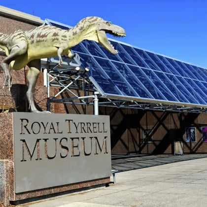 A dinosaur statue above the "Royal Tyrrell Museum" sign, with rows of large glass panels on the adjacent building.