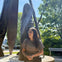 A person sits near a statue outdoors, with sunlight filtering through trees in the background.