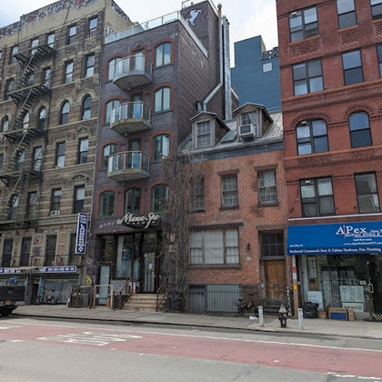 A city street view showing a row of multi-story buildings with storefronts on the ground floor and apartments above.