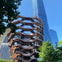 A modern architectural structure with a honeycomb-like design stands in front of a tall glass skyscraper under a clear blue sky.