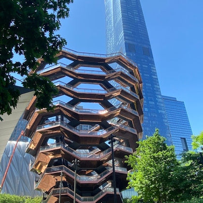 A modern architectural structure with a honeycomb-like design stands in front of a tall glass skyscraper under a clear blue sky.