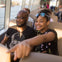 A man and a girl sitting on a boat, with the girl pointing forward and smiling. The background shows water and other passengers.