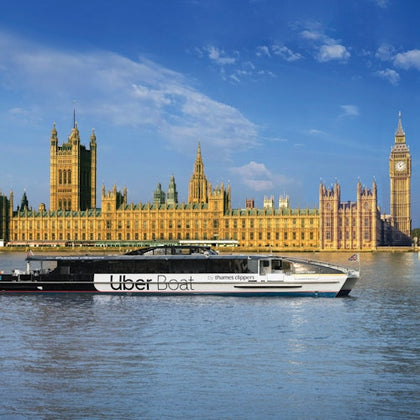 A boat labeled 'Uber Boat by Thames Clippers' on the River Thames, with the Houses of Parliament and Big Ben in the background.
