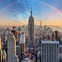View of a city skyline with the Empire State Building centered, other skyscrapers around, and a partial rainbow arching over.