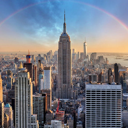 View of a city skyline with the Empire State Building centered, other skyscrapers around, and a partial rainbow arching over.
