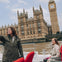 Two people on a boat ride on the Thames River with the Palace of Westminster and Big Ben visible in the background.