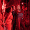 Three friends take a selfie in a dimly lit, red-hued room filled with hanging net decorations.