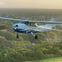 A small blue and white propeller airplane flying over a forested area at sunset, with the plane's registration number N4325R visible.