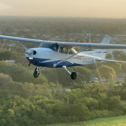 A small blue and white propeller airplane flying over a forested area at sunset, with the plane's registration number N4325R visible.