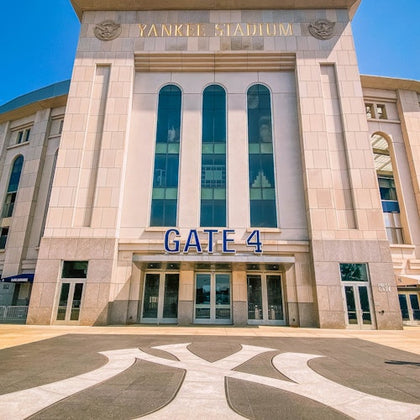 Entrance to Yankee Stadium, showcasing Gate 4 with large glass windows and the iconic Yankees logo on the ground.