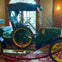 A vintage green automobile with yellow accents displayed in a room with ornate decor and a window in the background.