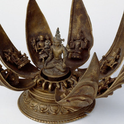 A bronze sculpture of a deity seated in a lotus surrounded by intricate depictions of other figures on the petals.