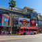 A red double-decker sightseeing bus on a city street, passing by buildings including the Hard Rock Cafe and TCL Chinese Theatre.