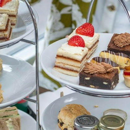 A three-tiered stand holding assorted pastries, sandwiches, and scones, with small jars of jam and cream.