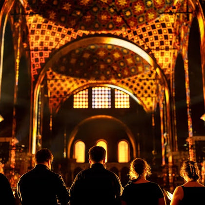 Five people in silhouette facing a brightly lit, ornate cathedral interior with colorful patterns and arched windows.