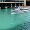 A white tour boat named 'Summer of George' on a turquoise river near a building with docks.