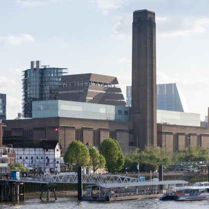 A riverside view of the Tate Modern art gallery in London, with the Globe Theatre and boats on the Thames in the foreground.