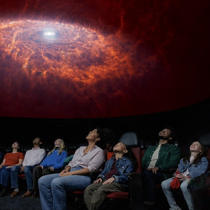 A group of people seated in a planetarium, looking up at a vivid depiction of a galaxy displayed on the dome ceiling.