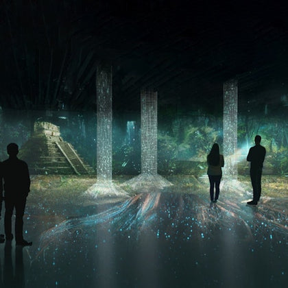 Silhouettes of people in a dark room with illuminated pillars and a projection of a jungle scene with a pyramid structure.