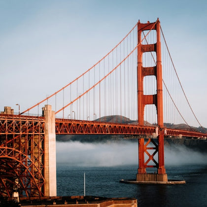 The Golden Gate Bridge spanning over water, with fog partially covering the background and clear skies above.