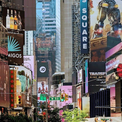 A busy urban area with numerous colorful billboards, advertisements, and traffic lights, surrounded by tall buildings.