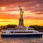 A ferry labeled 'NY Waterway' passes in front of the Statue of Liberty during a vibrant sunset.